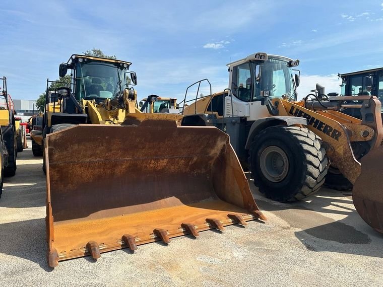 Liebherr wheel loader with raised bucket beside a Caterpillar wheel loader